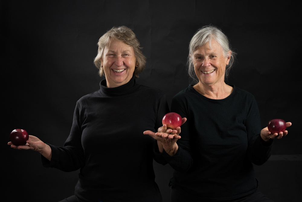 Two ladies dressed in black holding red apples